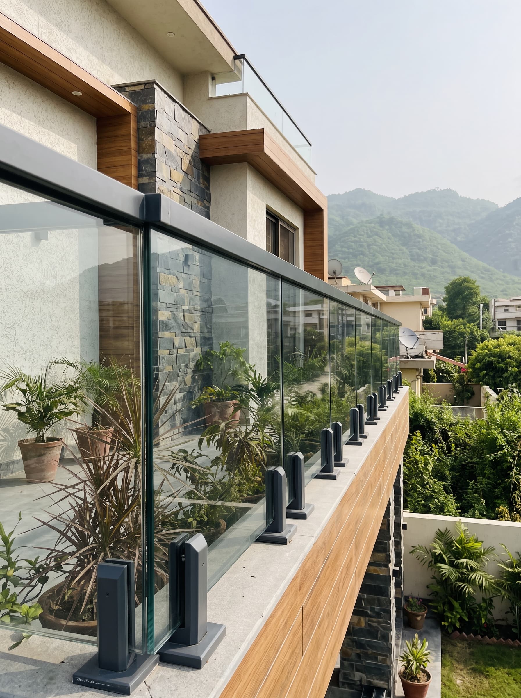 Frameless glass railing in black fittings along a terrace, with hills beyond