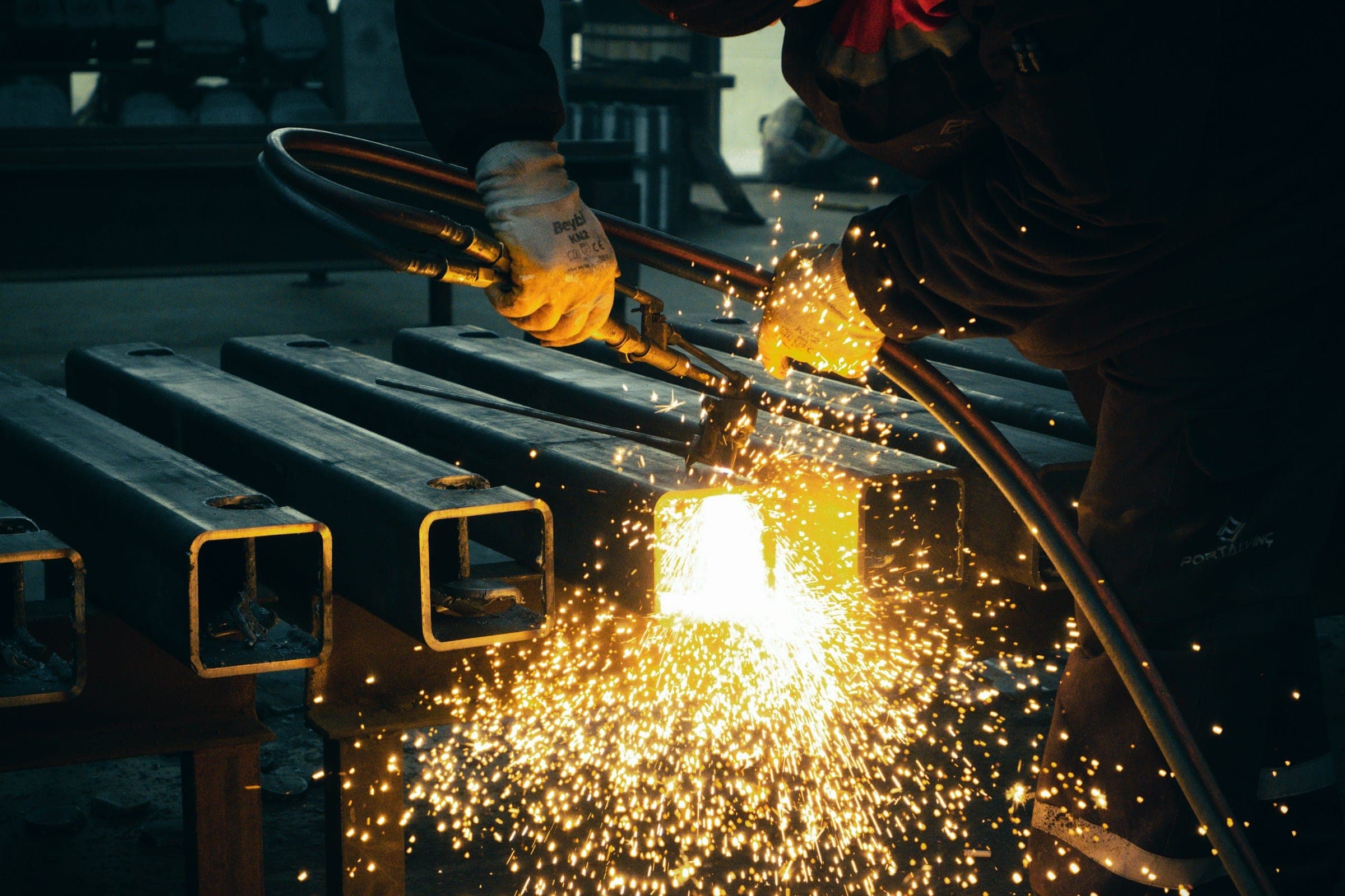Square steel pipe being cut in a fabrication workshop, sparks flying